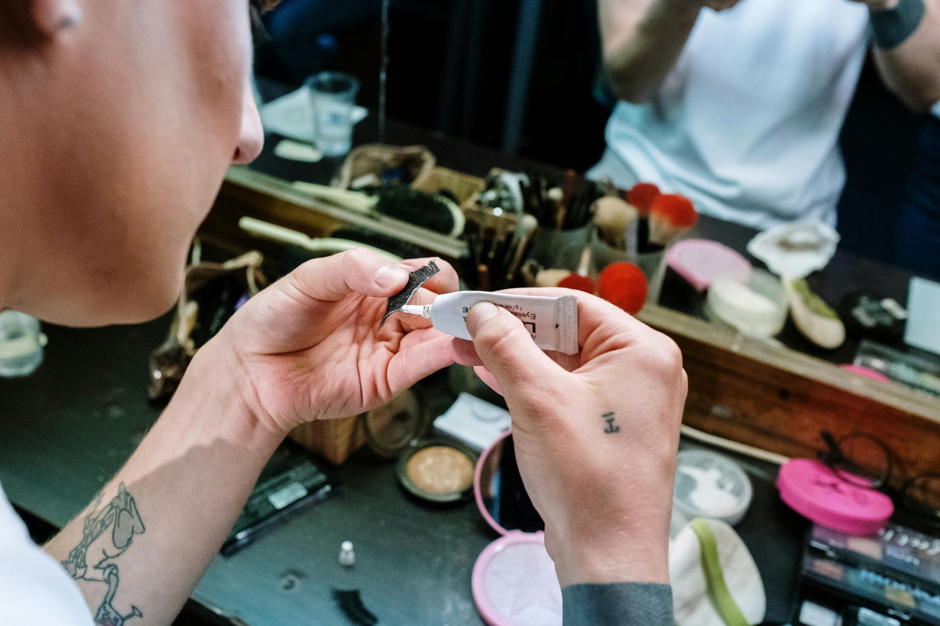 A woman with a tattoo on her arm is applying makeup in front of a mirror.