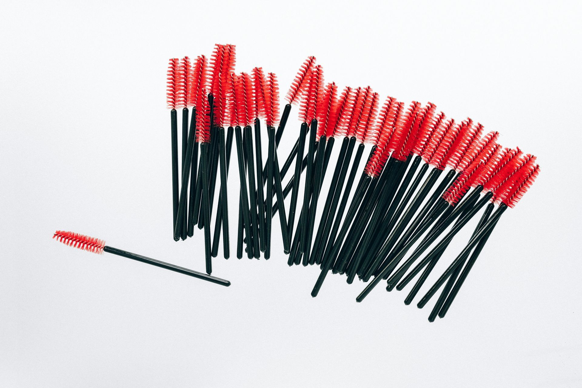 A bunch of red and black mascara brushes on a white surface.