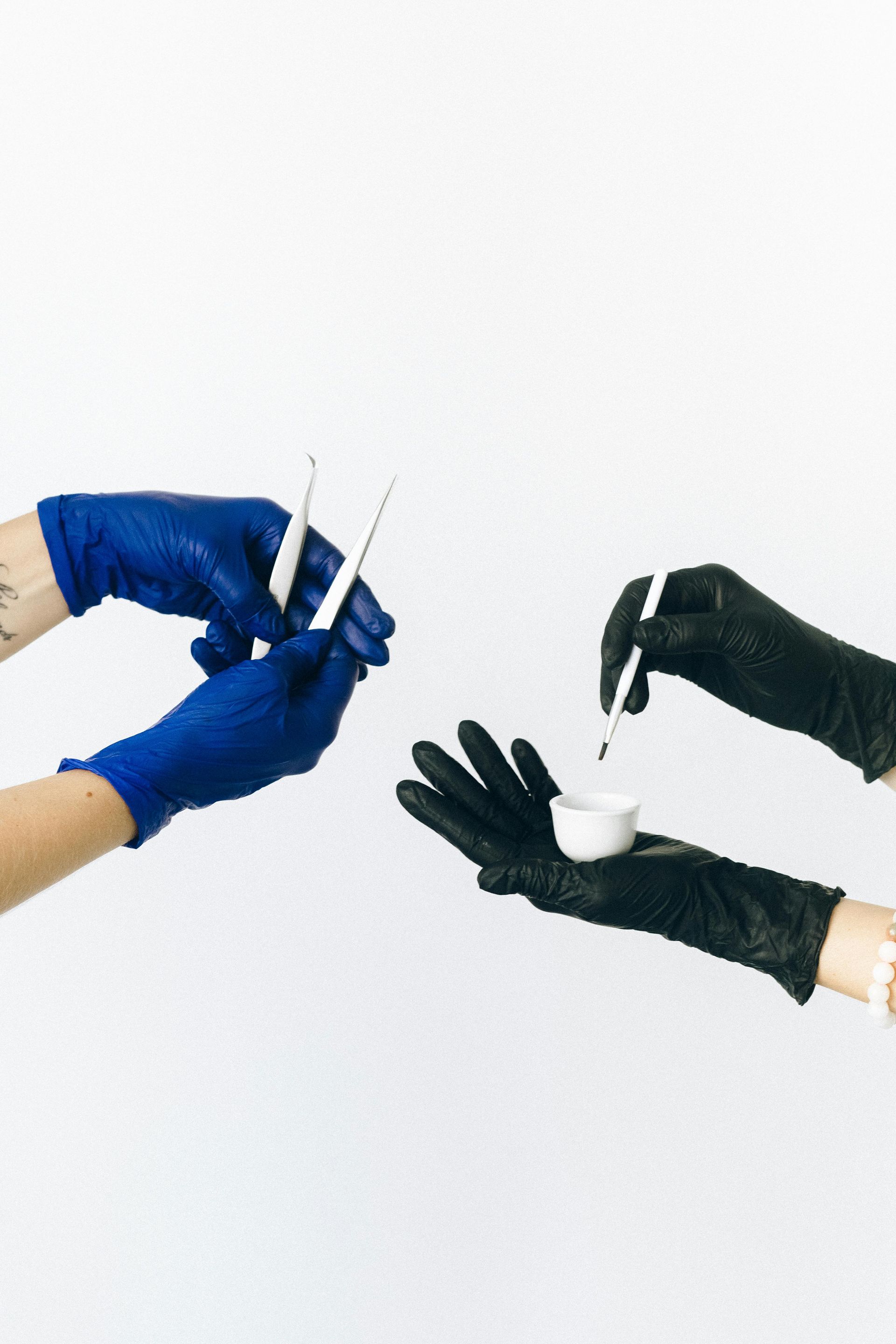 A person wearing blue gloves is holding a syringe and another person wearing black gloves is holding a pipette