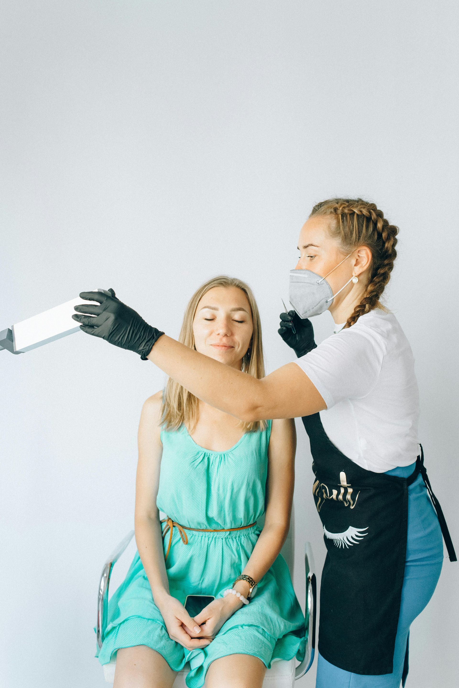A woman is getting her hair blow dried by a hairdresser while wearing a mask.