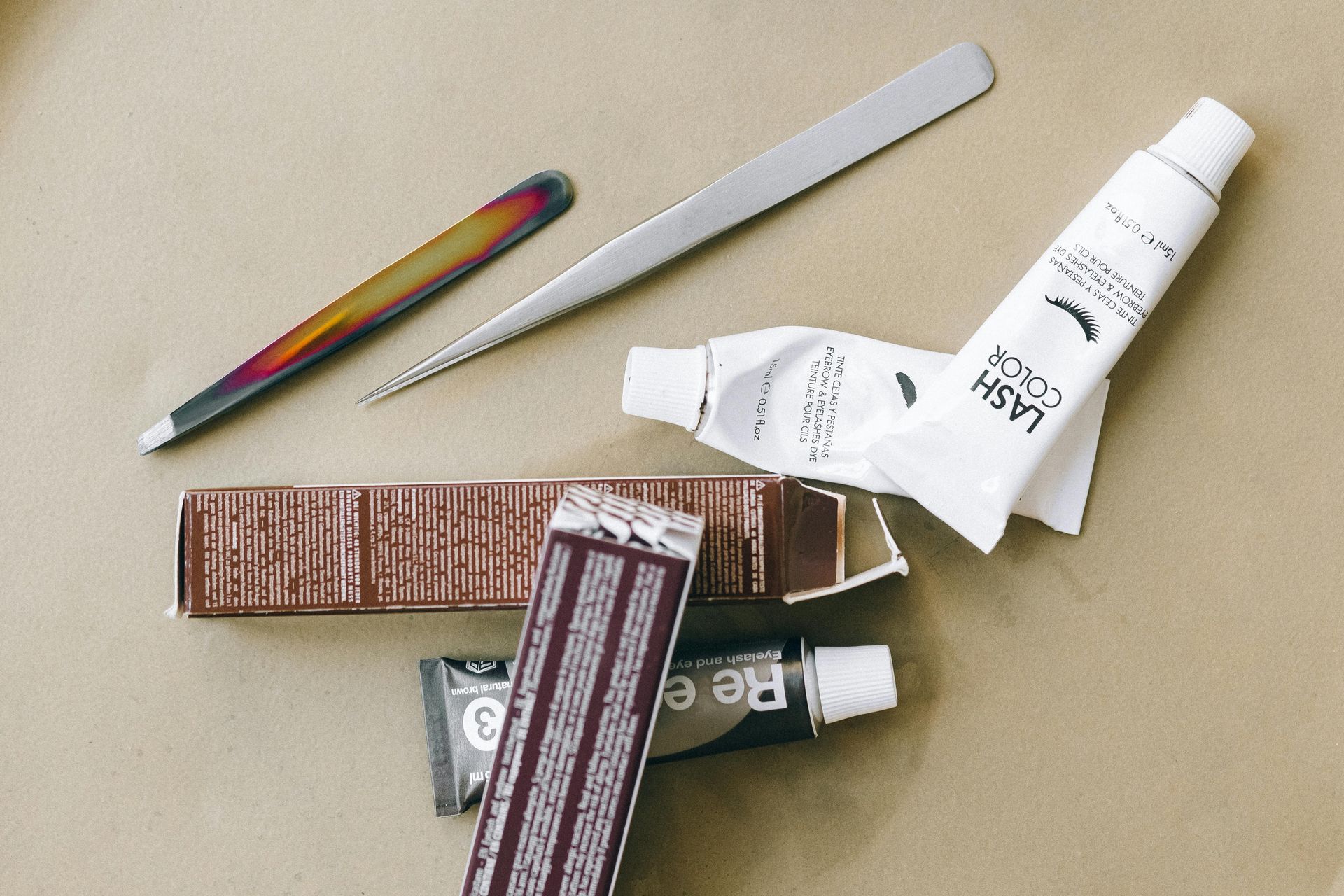 A pair of tweezers sitting next to a tube of lash color