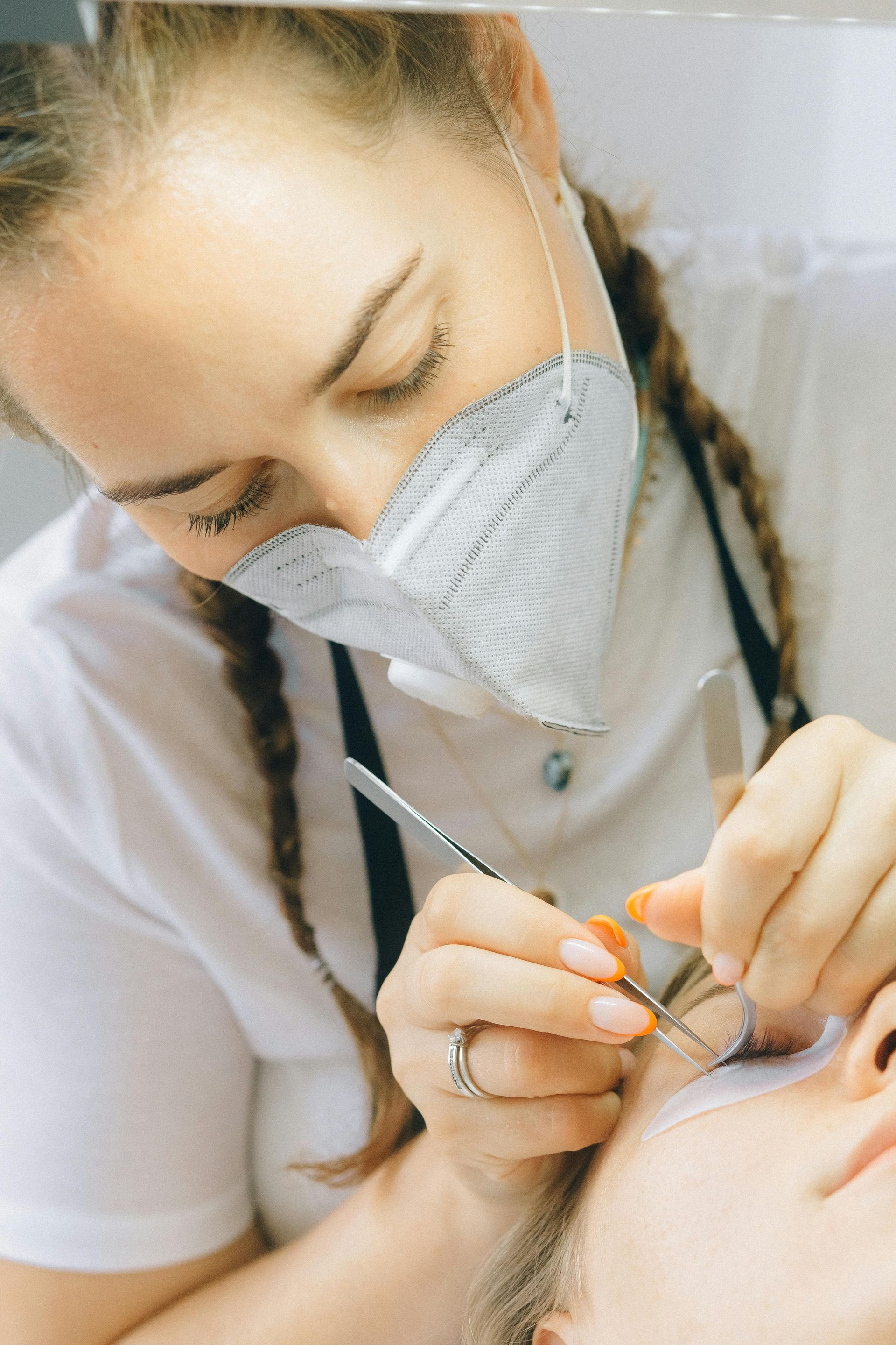 A woman wearing a mask is applying eyelash extensions to a woman 's eye.