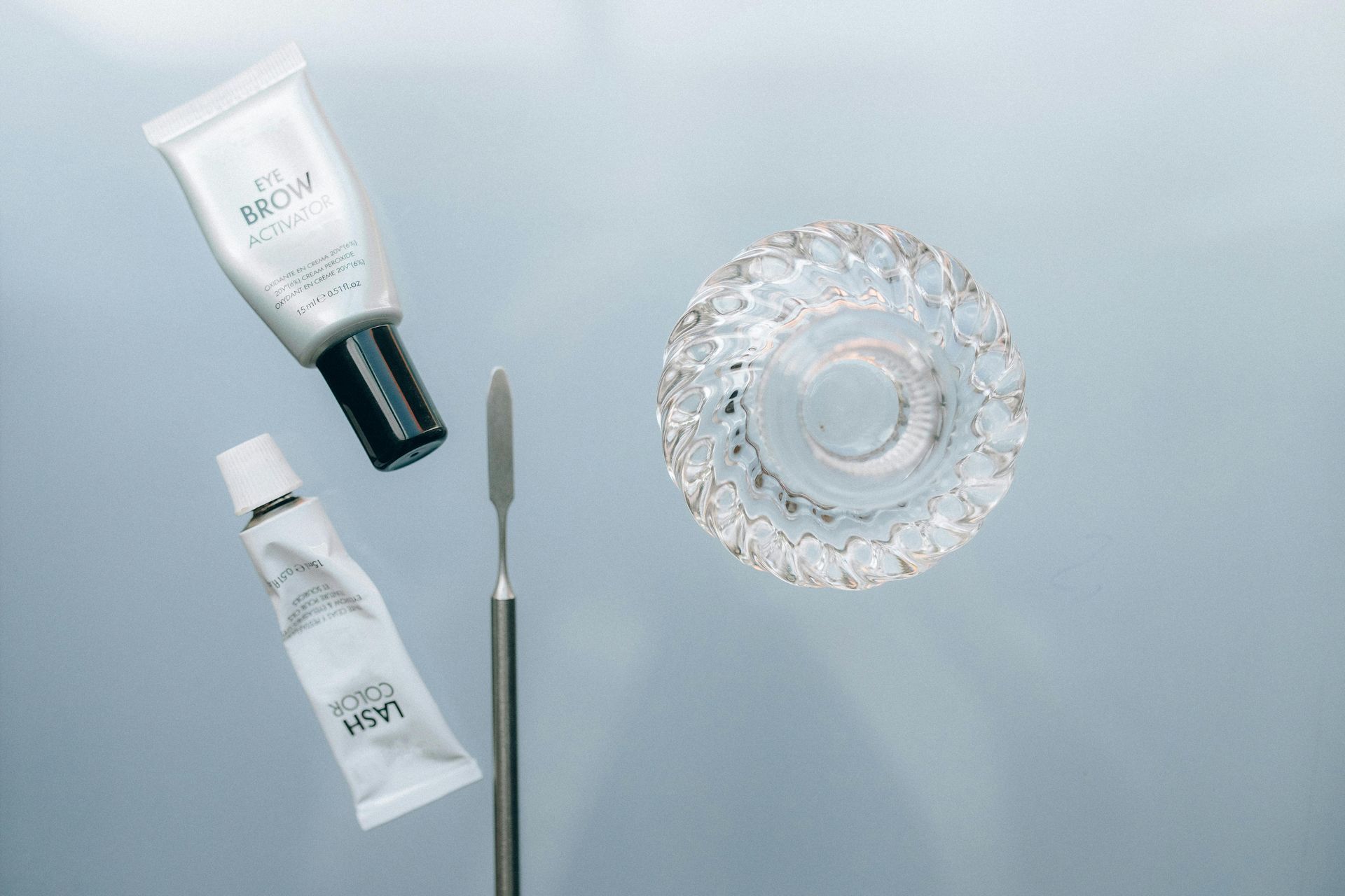 A bottle of lotion , a spatula , and a glass bowl on a table.