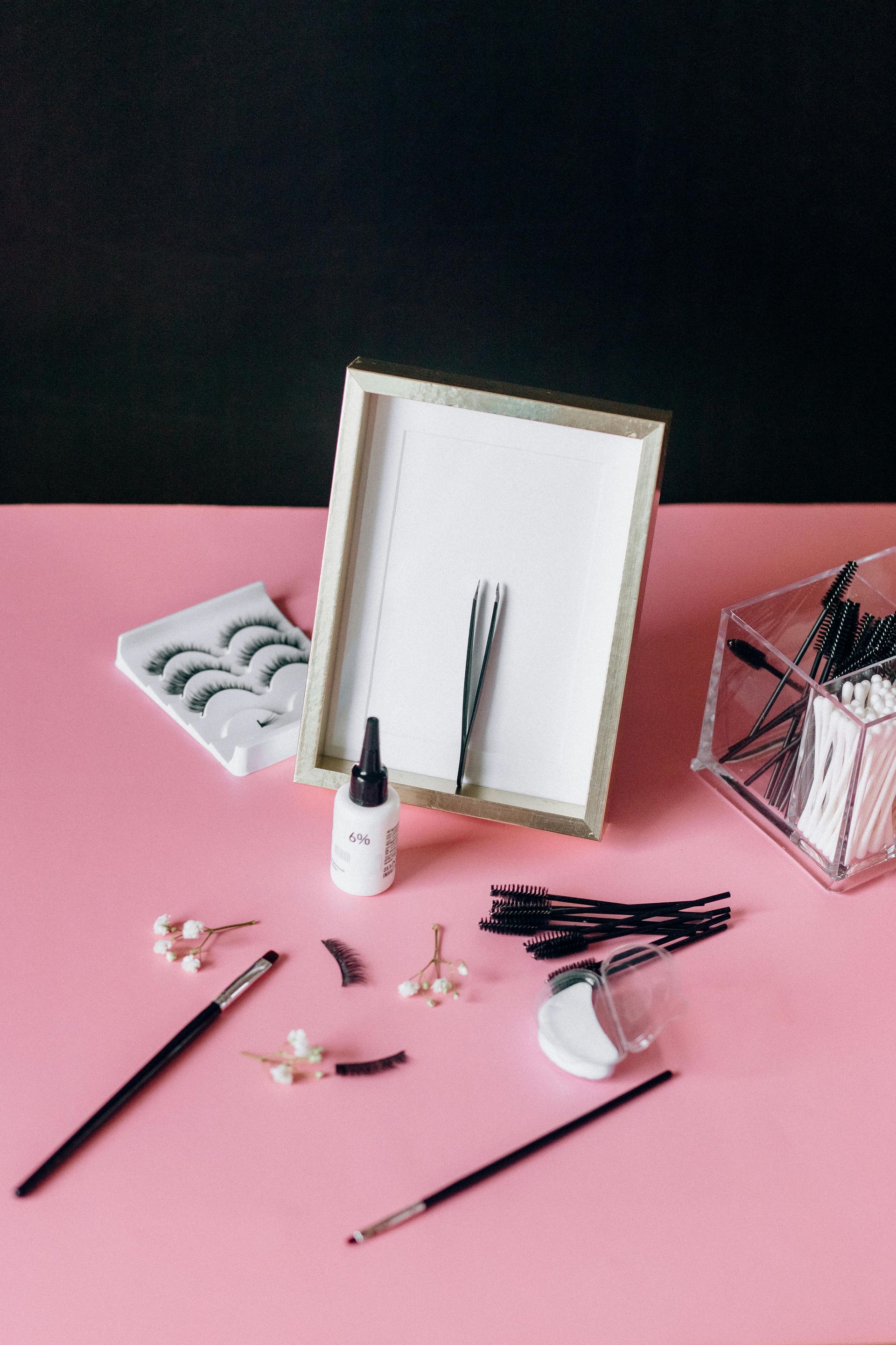 A pink table with a picture frame , brushes , and a bottle of glue.