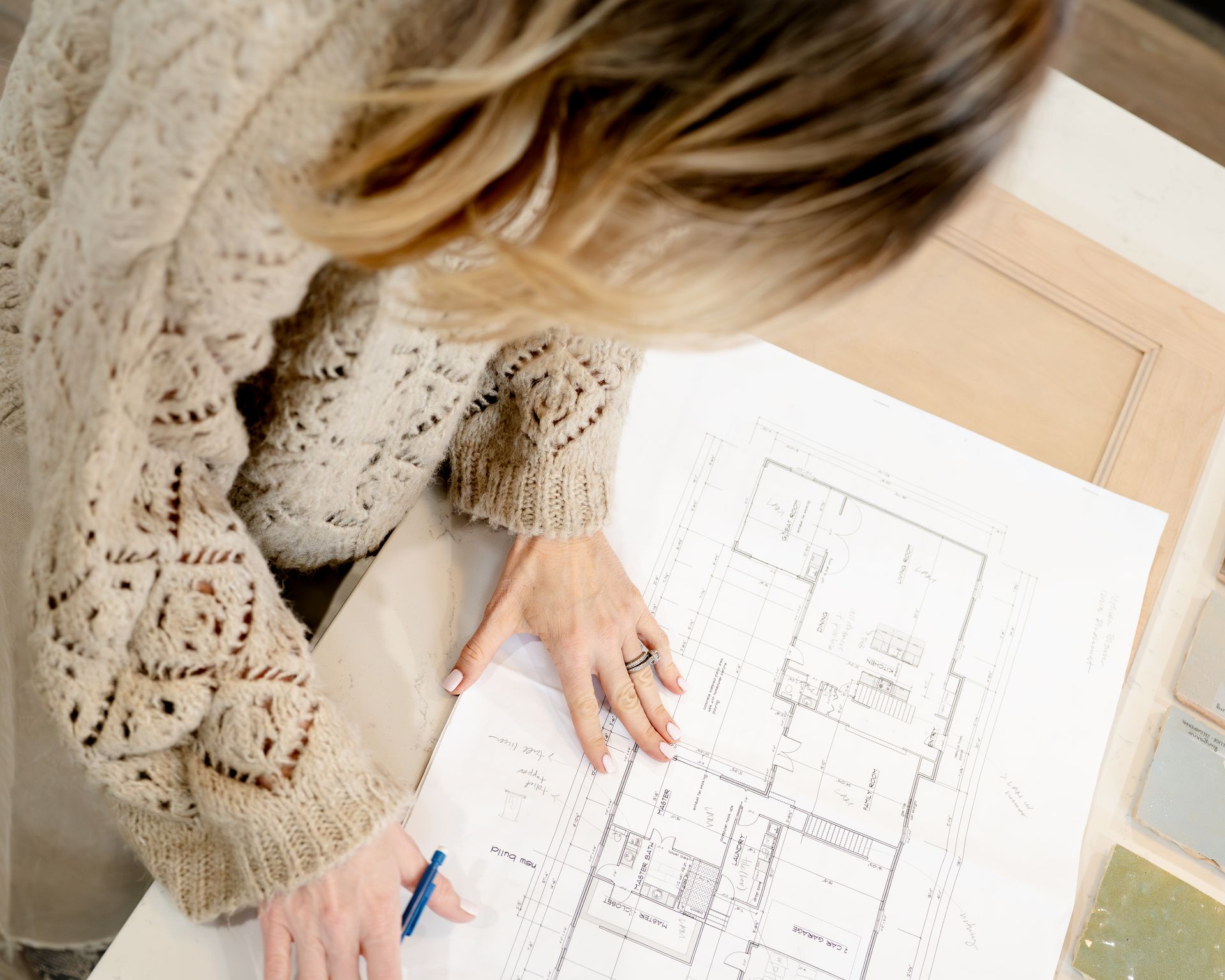 Woman in sweater examining floor plan, with paint swatches nearby.