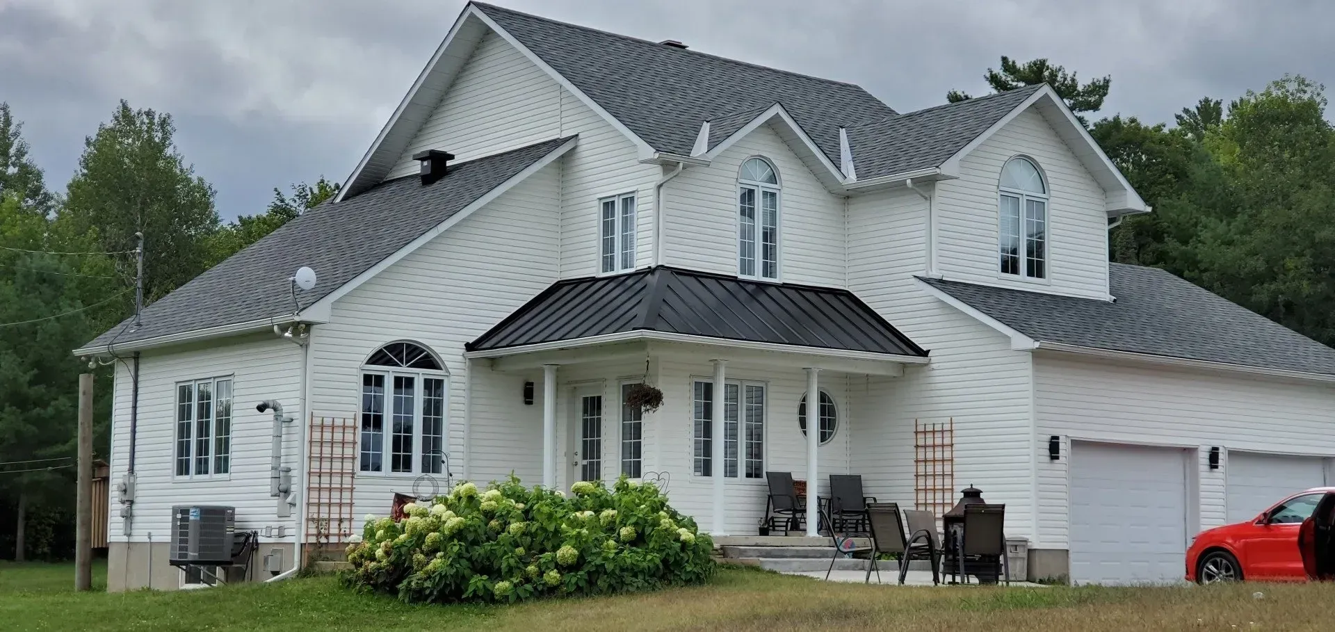 Une grande maison blanche avec une voiture rouge garée devant