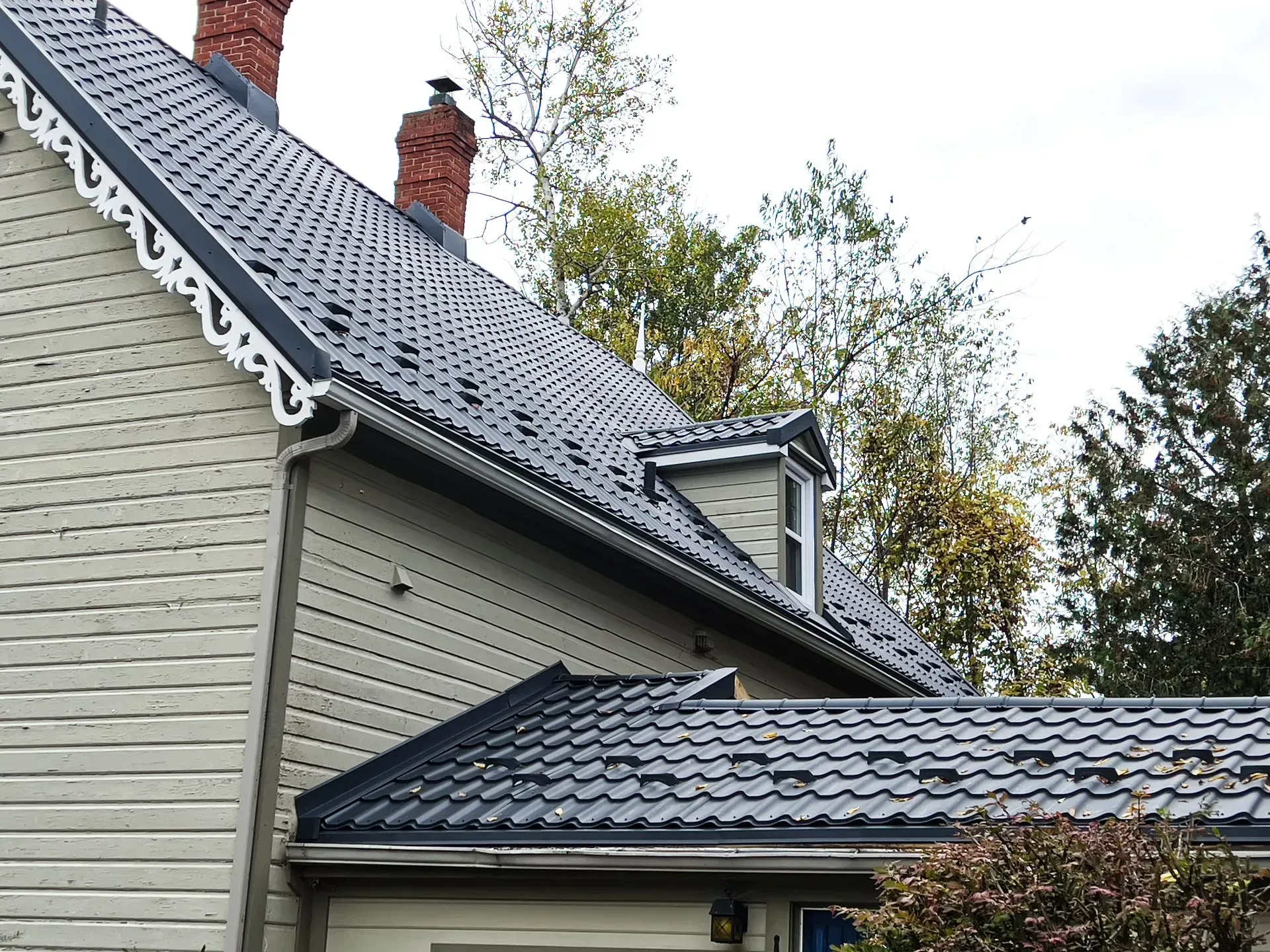 Une maison blanche avec un toit noir et une cheminée.