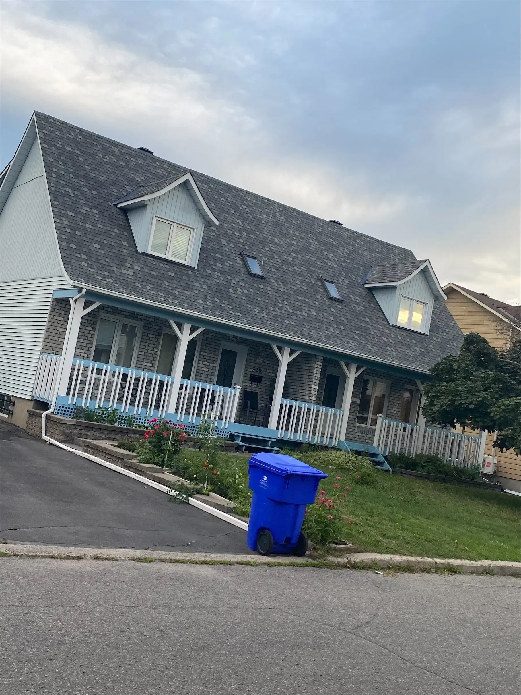 Une grande maison blanche avec une poubelle bleue devant.