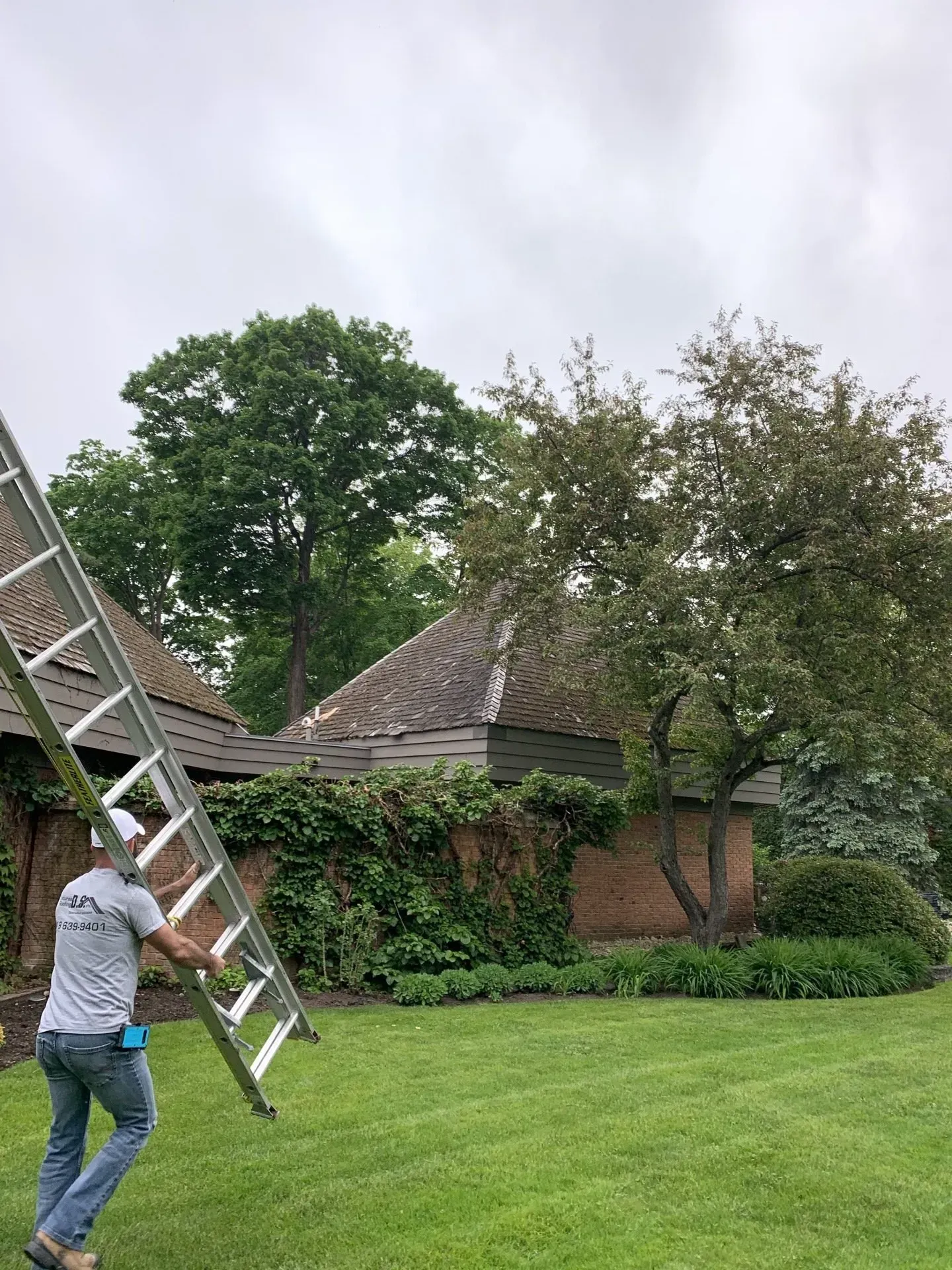 Un homme porte une échelle devant une maison.