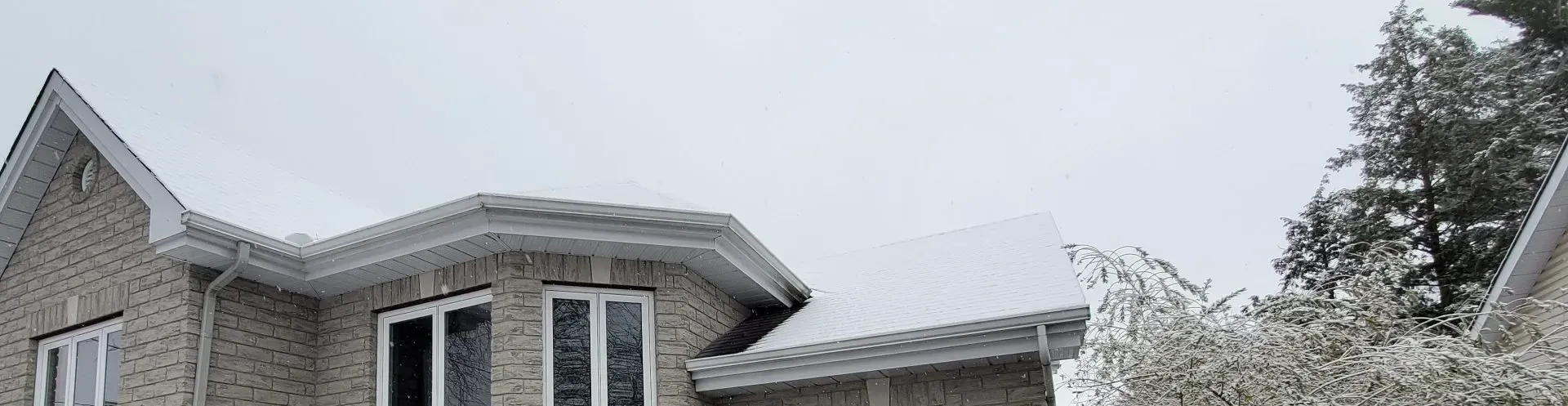 Une grande maison en brique avec de la neige sur le toit et des arbres en arrière-plan.