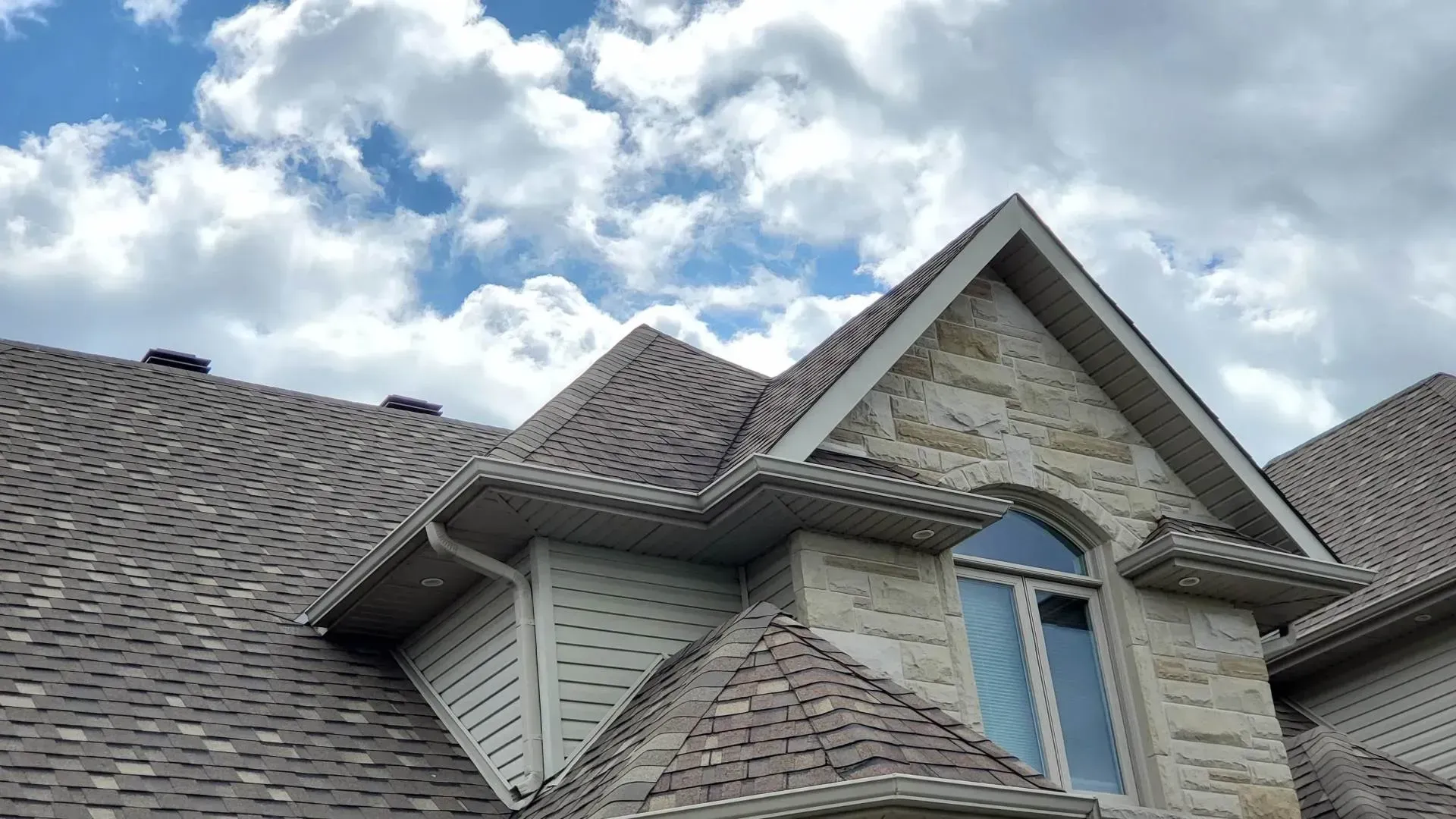 Le toit d'une maison avec une fenêtre et un ciel nuageux en arrière-plan.