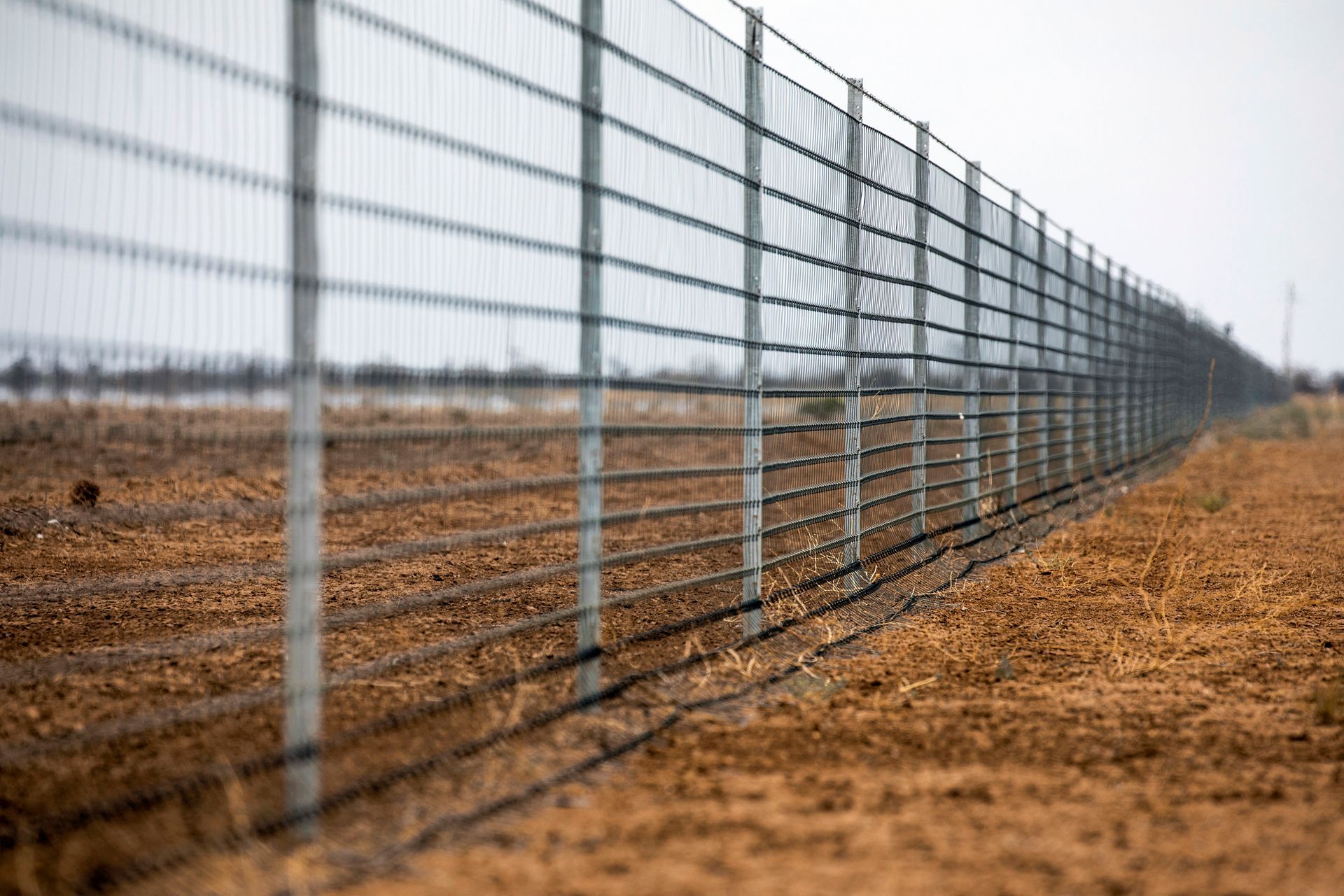 A long metal fence surrounds a dirt field.