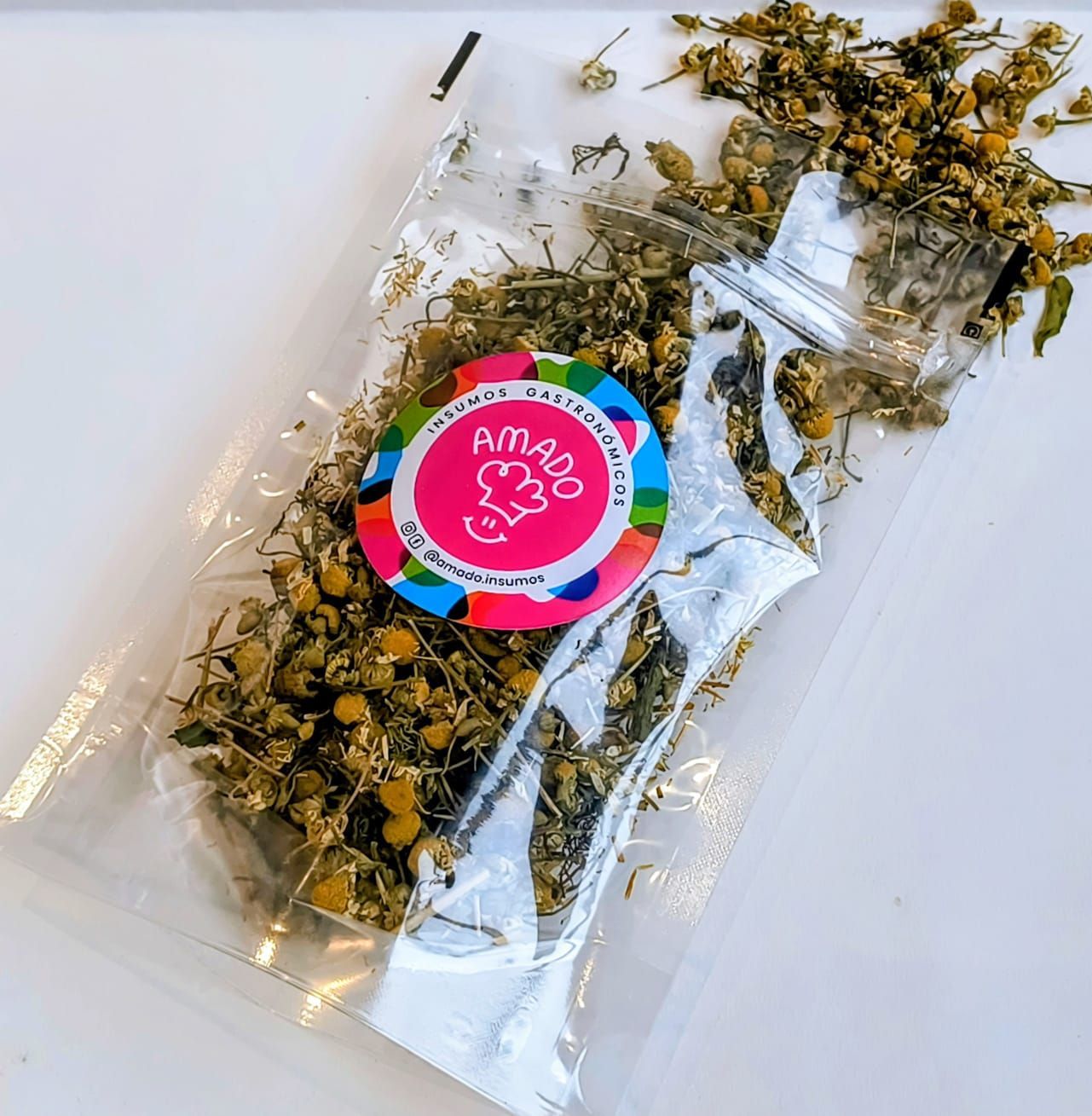 Té de manzanilla seco en una bolsa de plástico transparente con una etiqueta colorida sobre una superficie blanca.