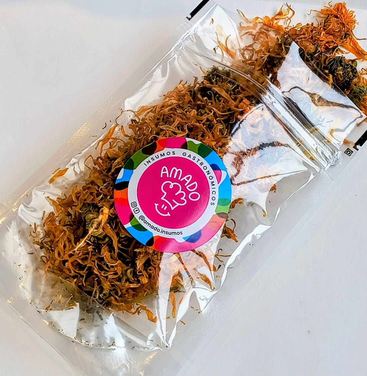 Bolsa de plástico transparente con alimento seco. Etiqueta con el texto "AMADO". Superficie blanca.