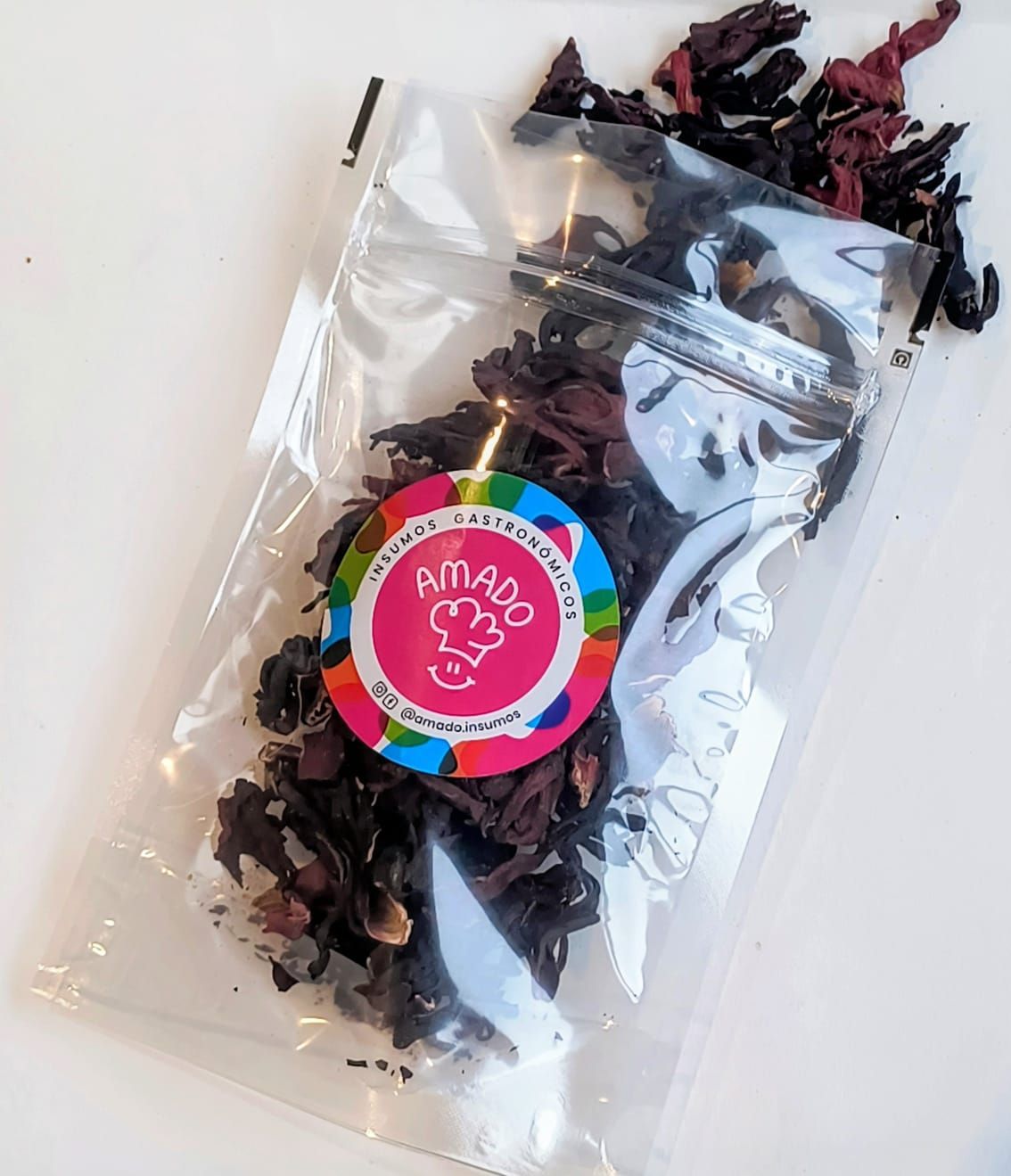 Bolsa de plástico transparente con flores de hibisco rojo secas y una etiqueta colorida que dice "Amado".