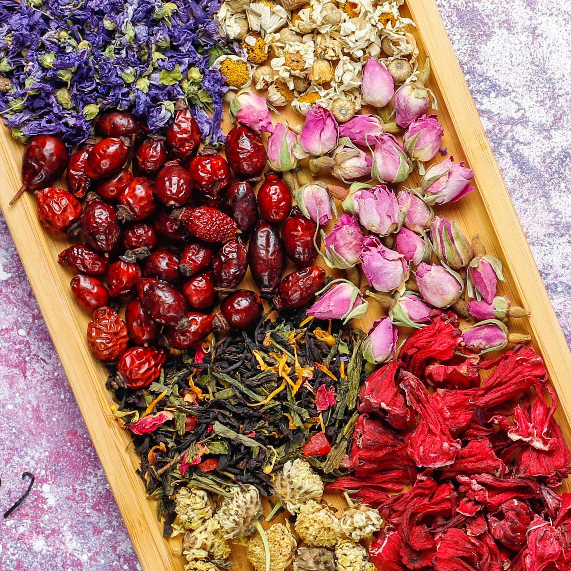 Bandeja de madera con una variedad de hierbas secas, flores y bayas, incluidos escaramujos, manzanilla e hibisco.