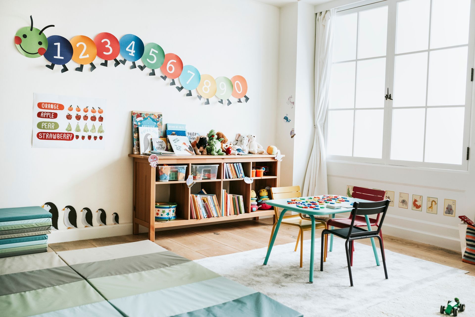a clean child 's room with a table and chairs and a caterpillar on the wall .