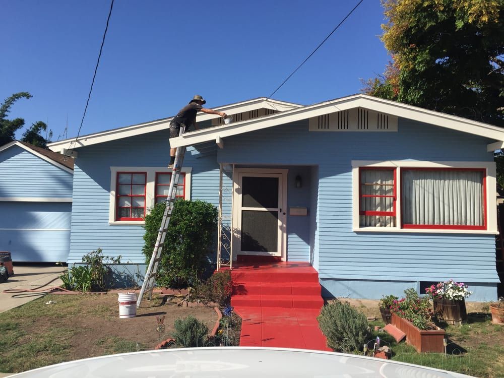 A man is painting the roof of a blue house