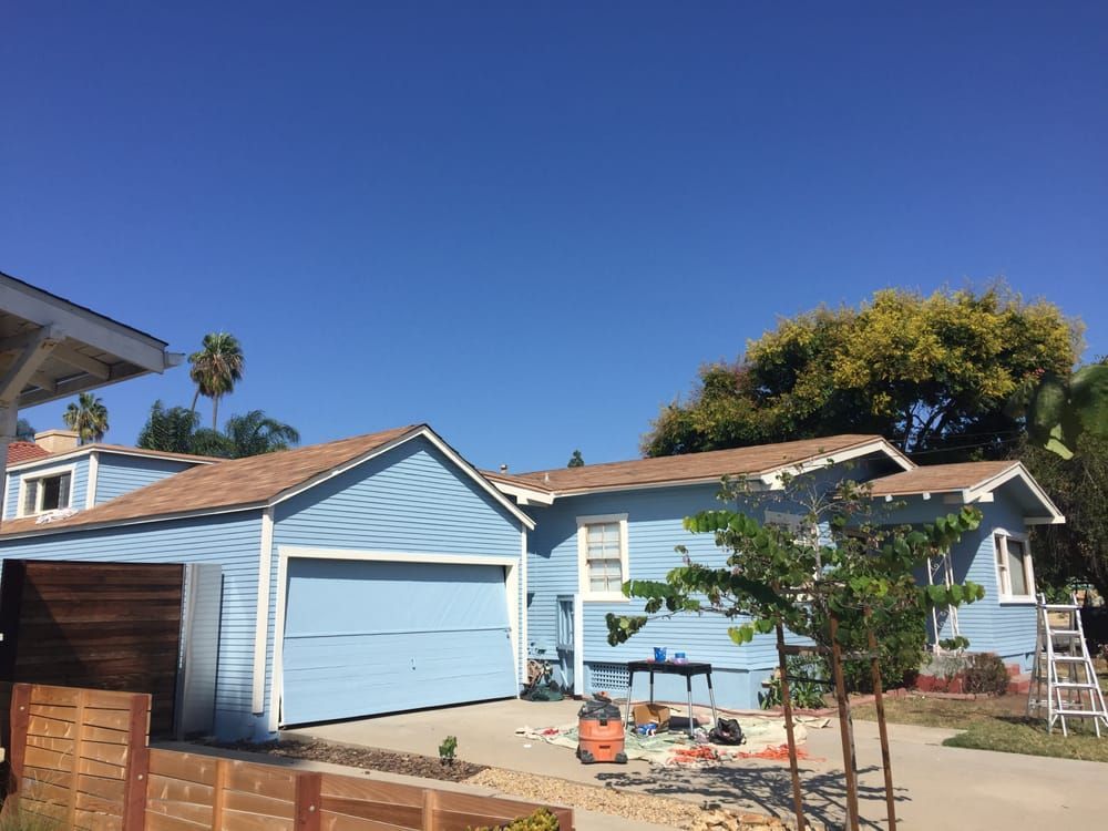 A blue house with a brown roof is being painted.