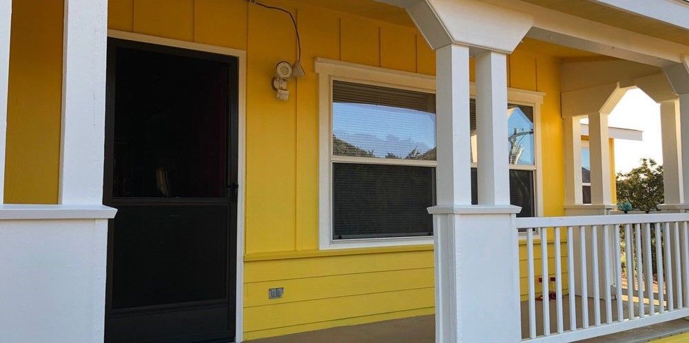 A yellow house with a white porch and a black door.