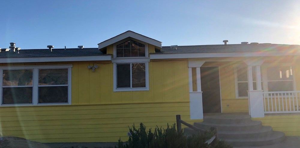 A yellow house with a white porch and a blue sky in the background.