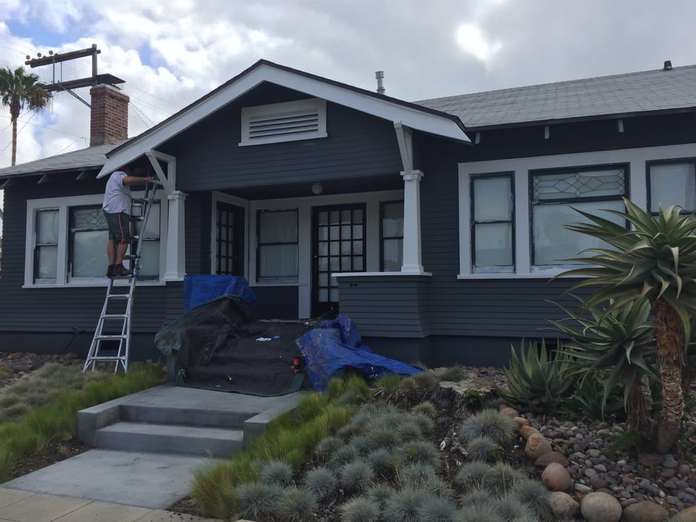 A man on a ladder is painting the front of a house