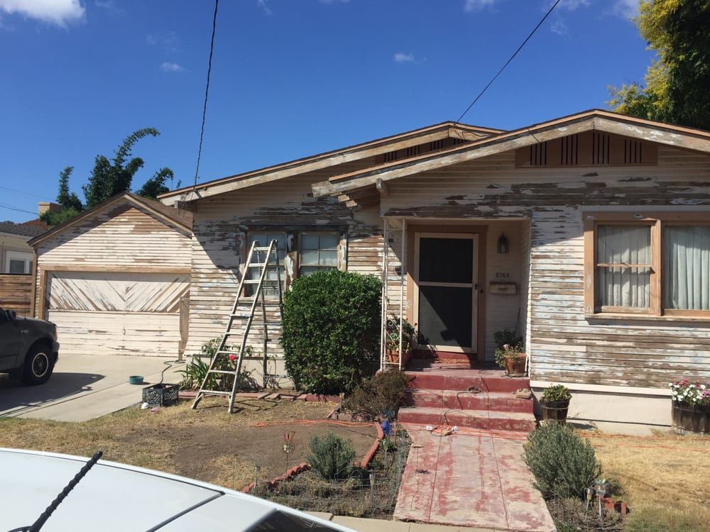 A house with a ladder in front of it and a car parked in front of it.