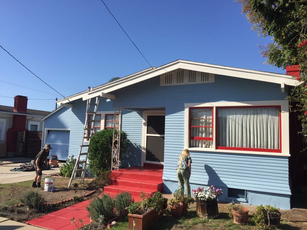 A woman is painting a blue house with red trim