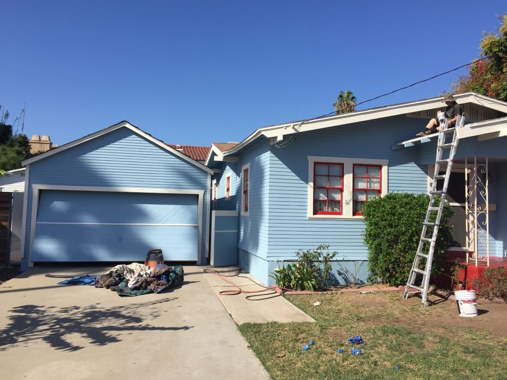 A blue house is being painted by a man on a ladder