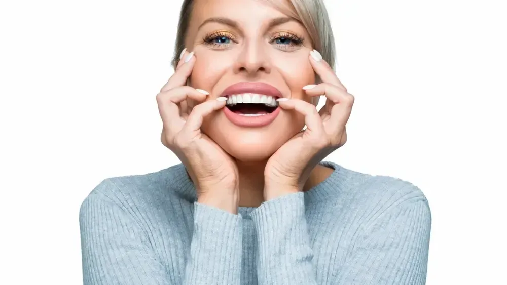 Woman with clear dental aligners in her mouth, smiling, holding cheeks.