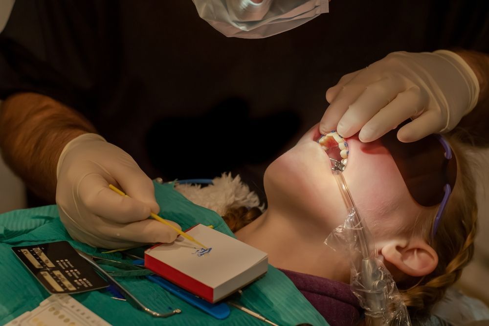 Dentist examining a child's mouth with tools; child lies back with mouth open.