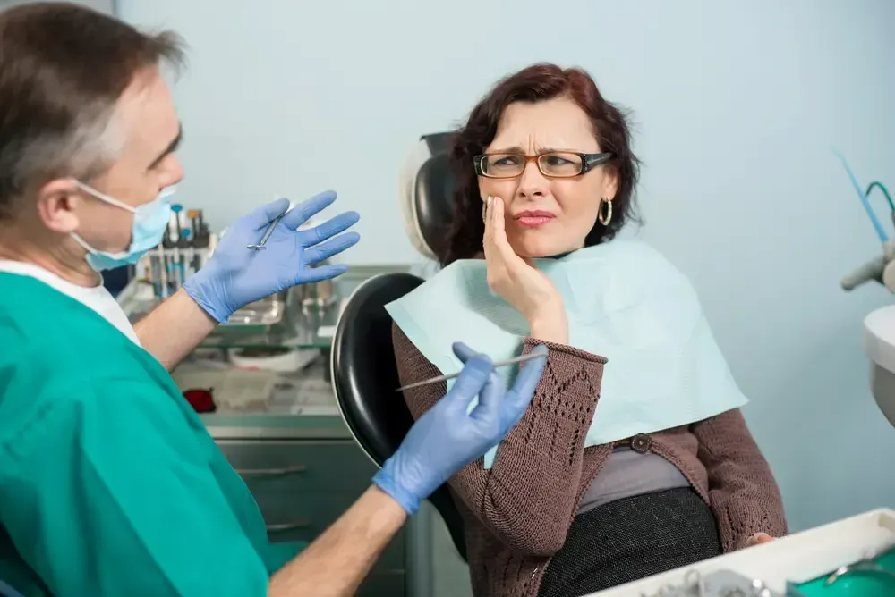 Dentist examining a patient with a hand on her cheek, showing distress in a dental office.