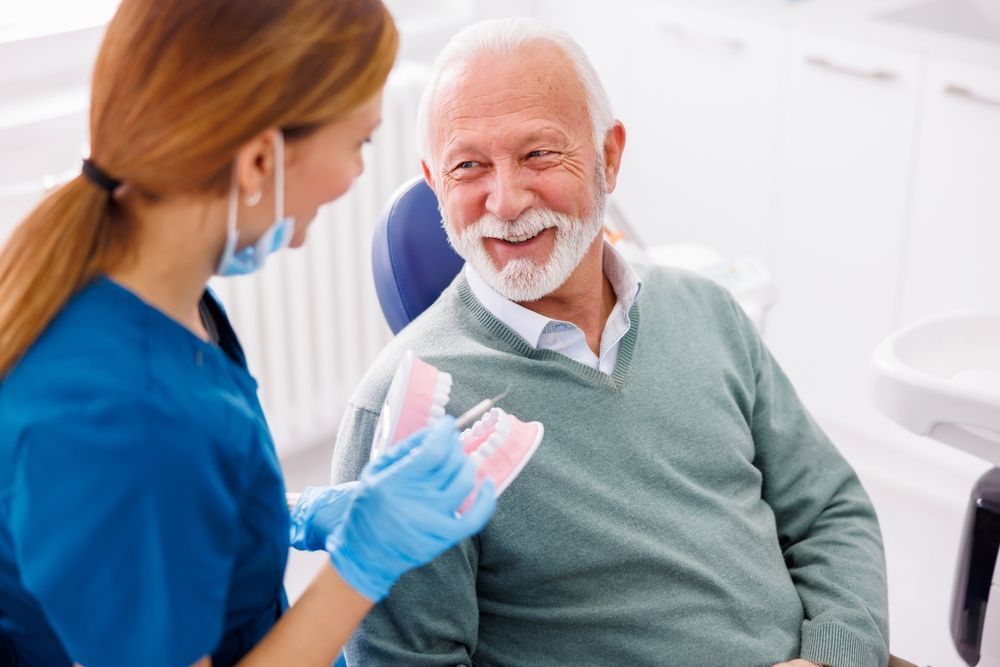 Dentist showing dentures to smiling elderly man in a dental office.