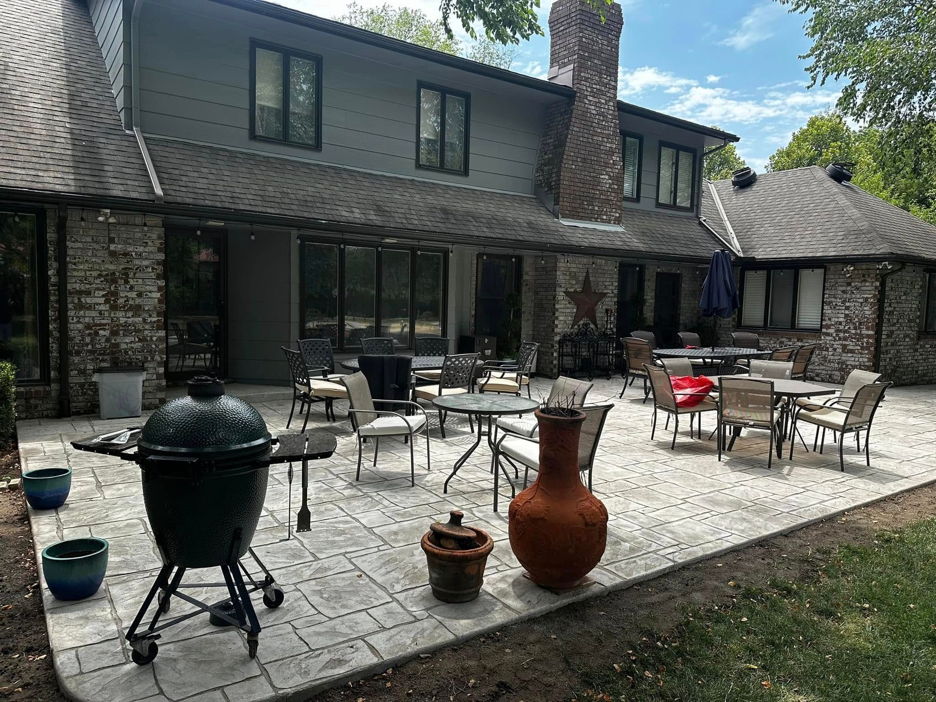 A large house with a patio with tables and chairs and a grill.