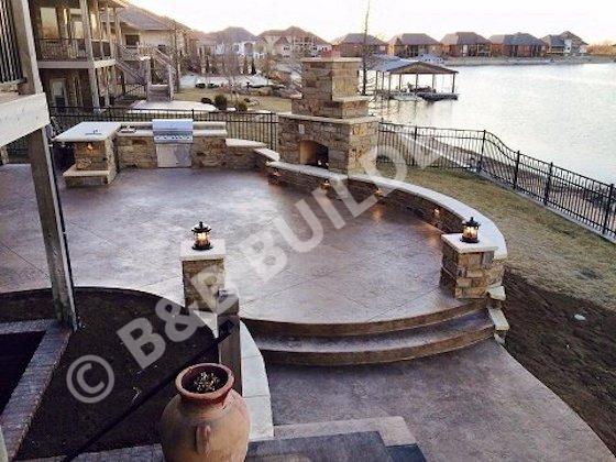 Round raised stamped concrete patio with stone seat walls, stone fireplace, and outdoor kitchen
