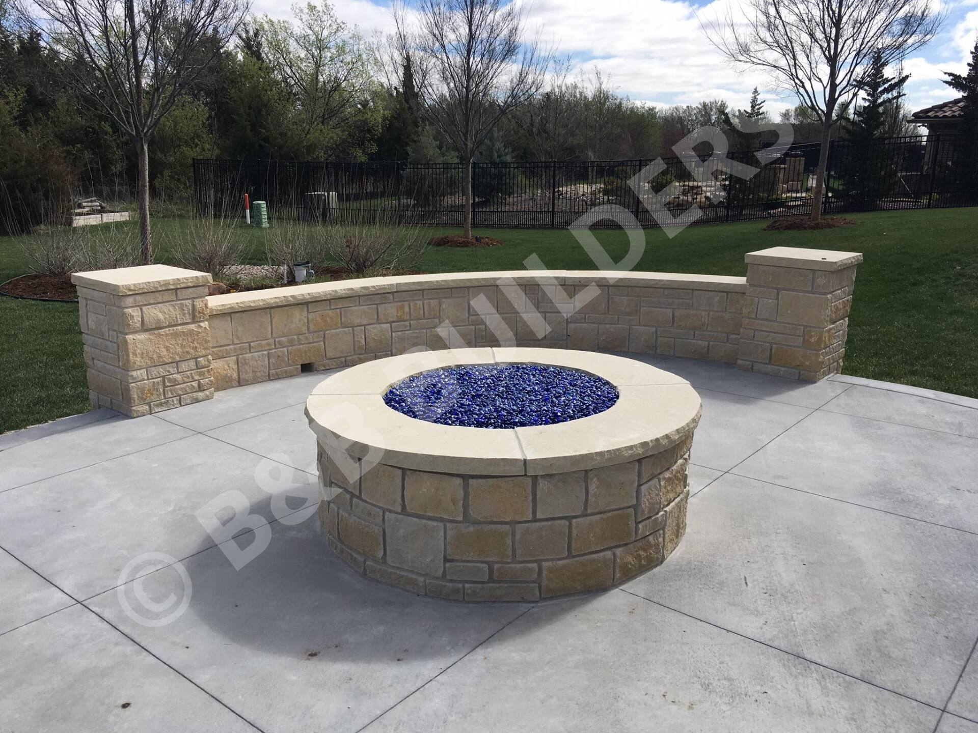 Round masonry firepit with blue glass fire area and sitting wall