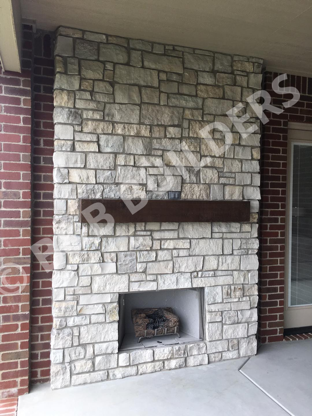 A stone fireplace on a brick wall, with inset thick timber mantel