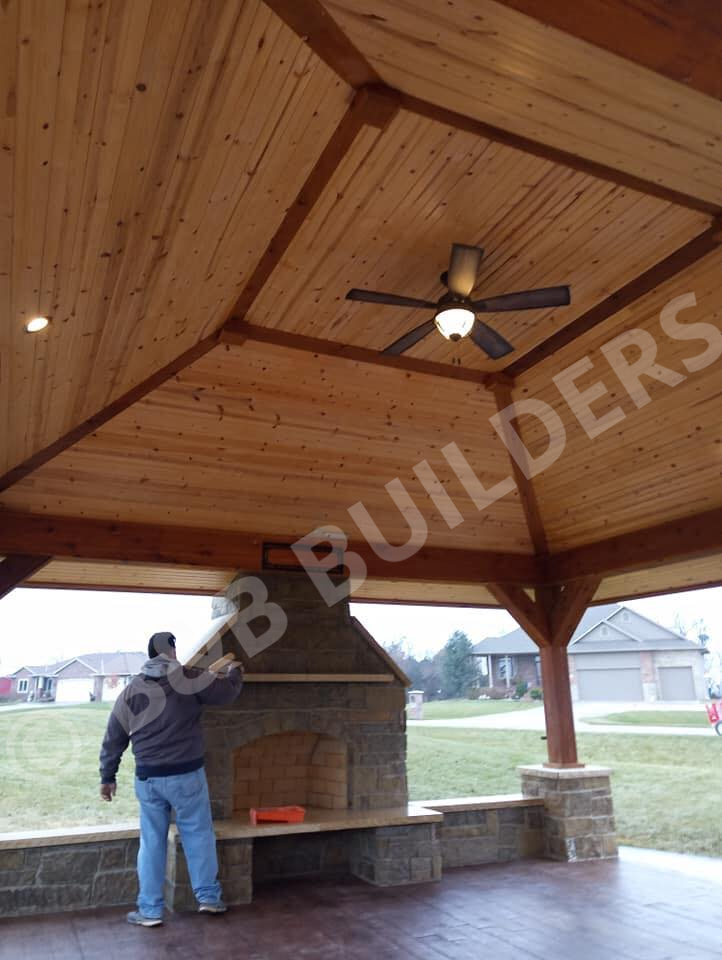 Stone outdoor fireplace with wood shelter and ceiling fan
