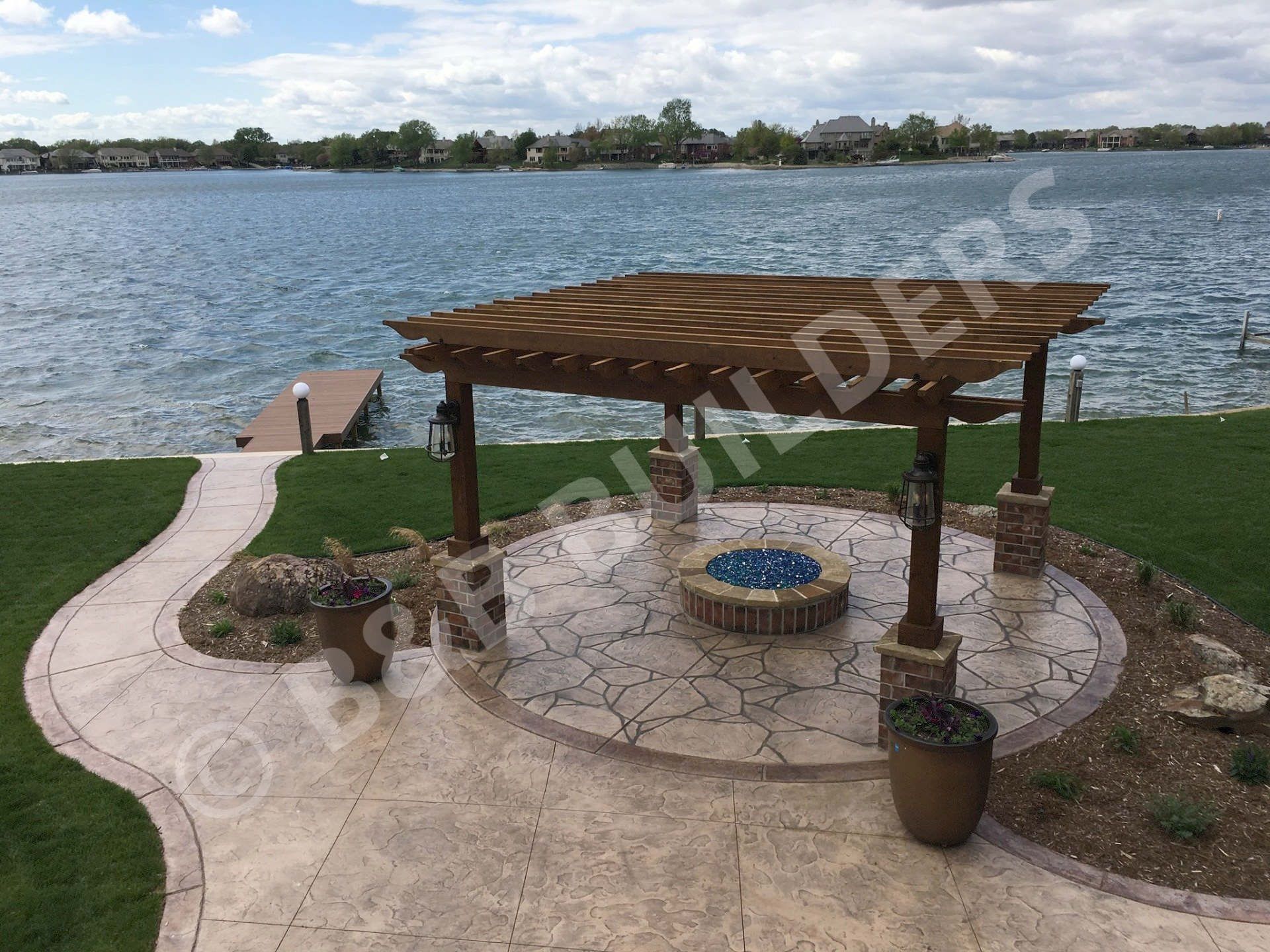 Stamped concrete patio with pergola, brick firepit with blue glass fire area