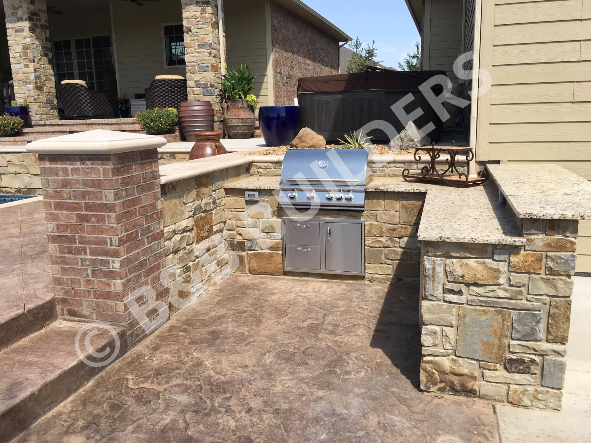 A grill inset into a bilevel stone bar with stamped concrete patio