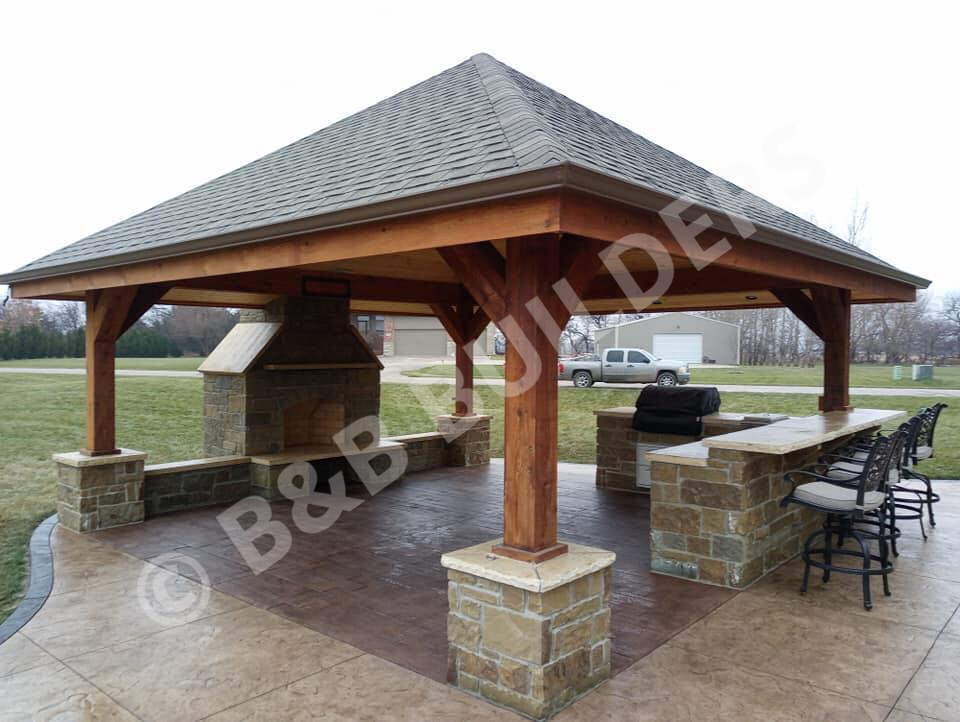 Roofed stone outdoor kitchen and fireplace on stamped concrete