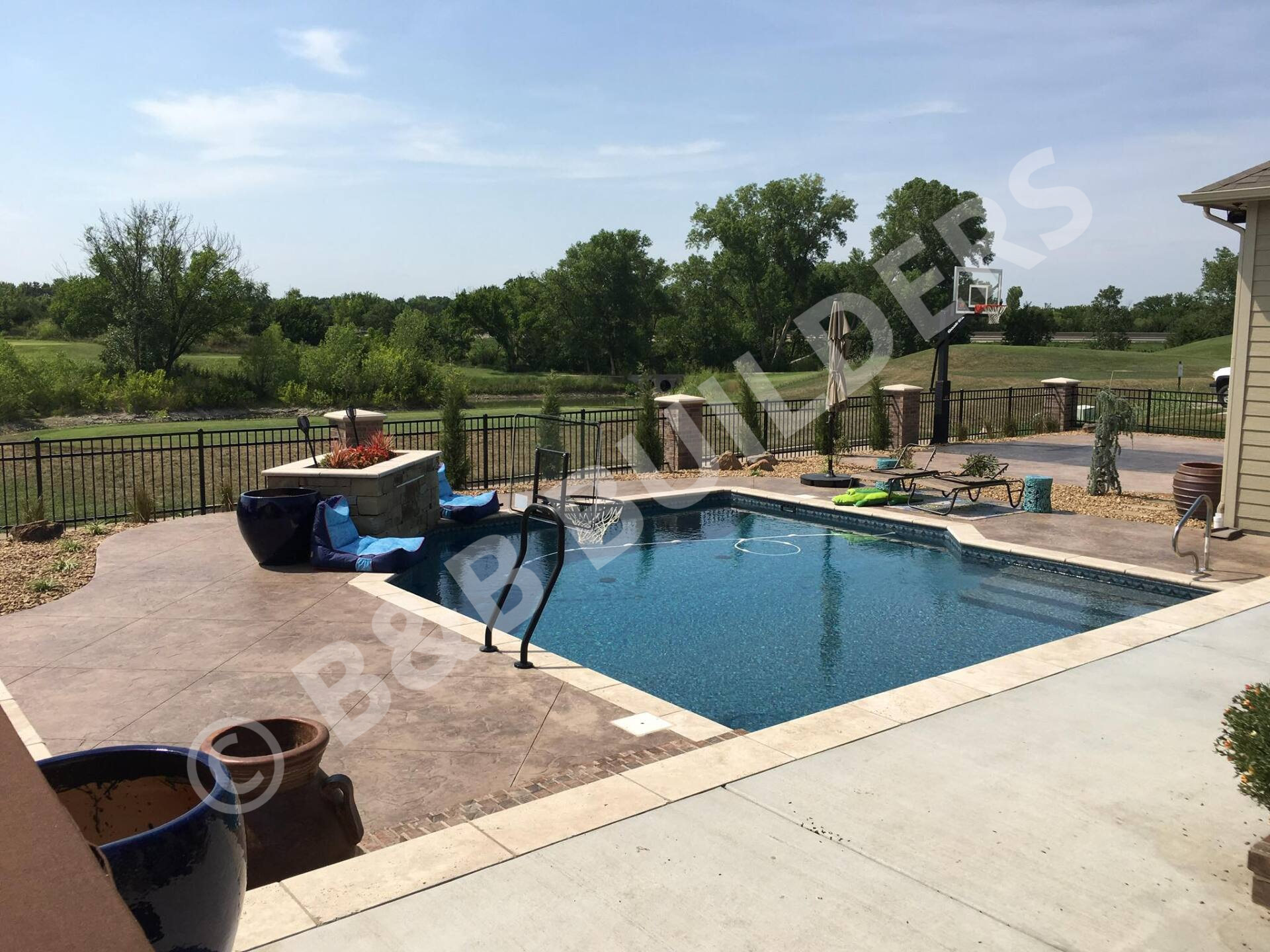 Rectangular pool with stamped and dyed concrete pool deck, firepit, and basketball court