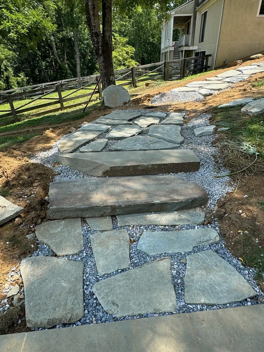 A stone walkway leading to a house with a fence in the background.