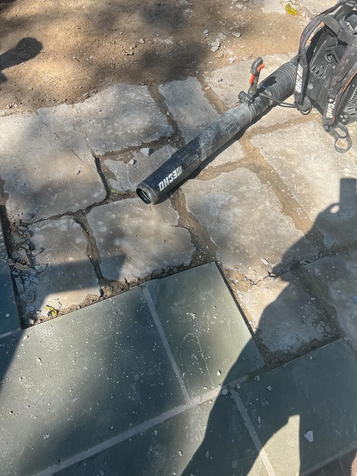 A person is standing next to a blower on a sidewalk.