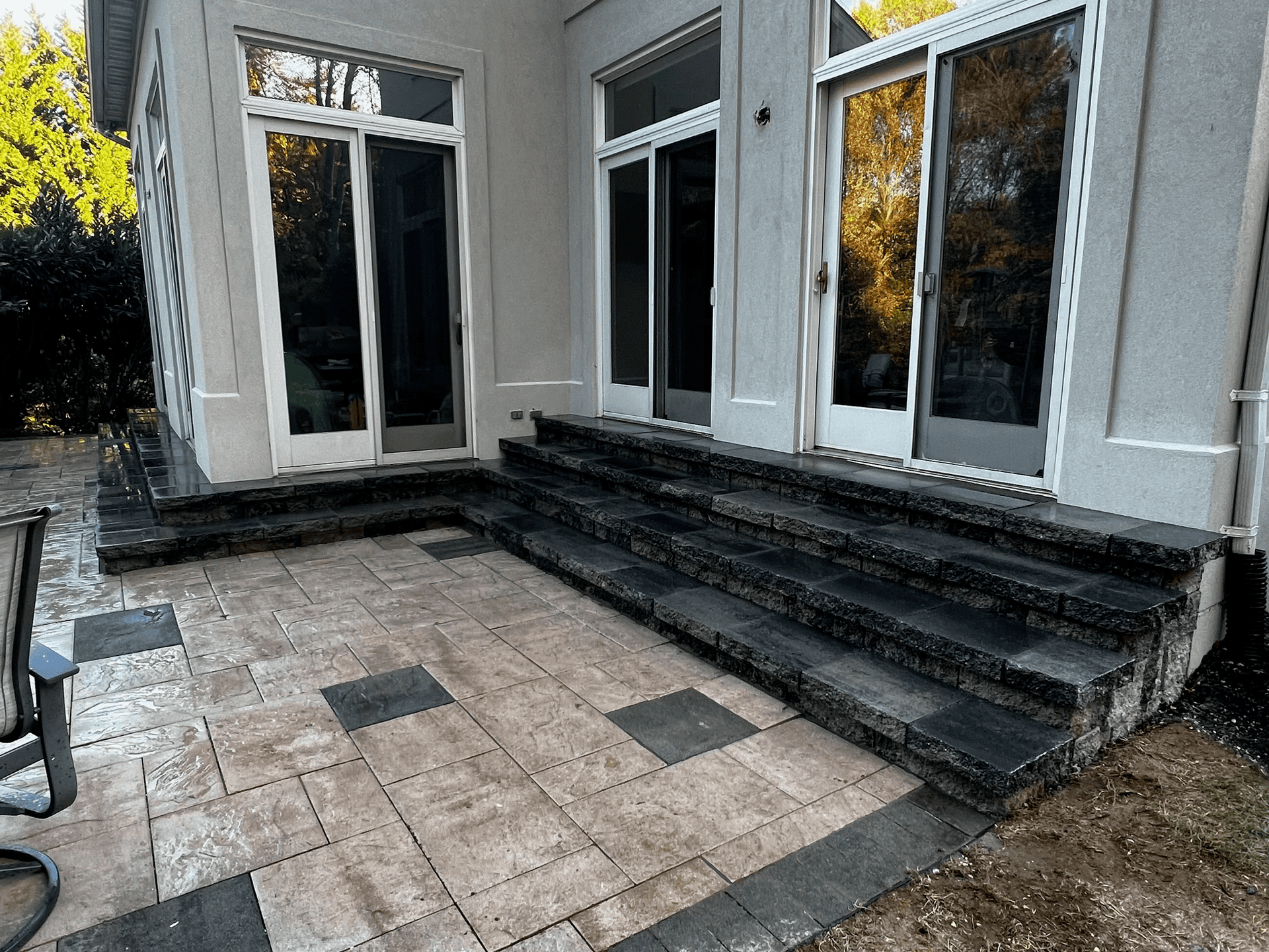 A patio with stairs leading up to a house with sliding glass doors.