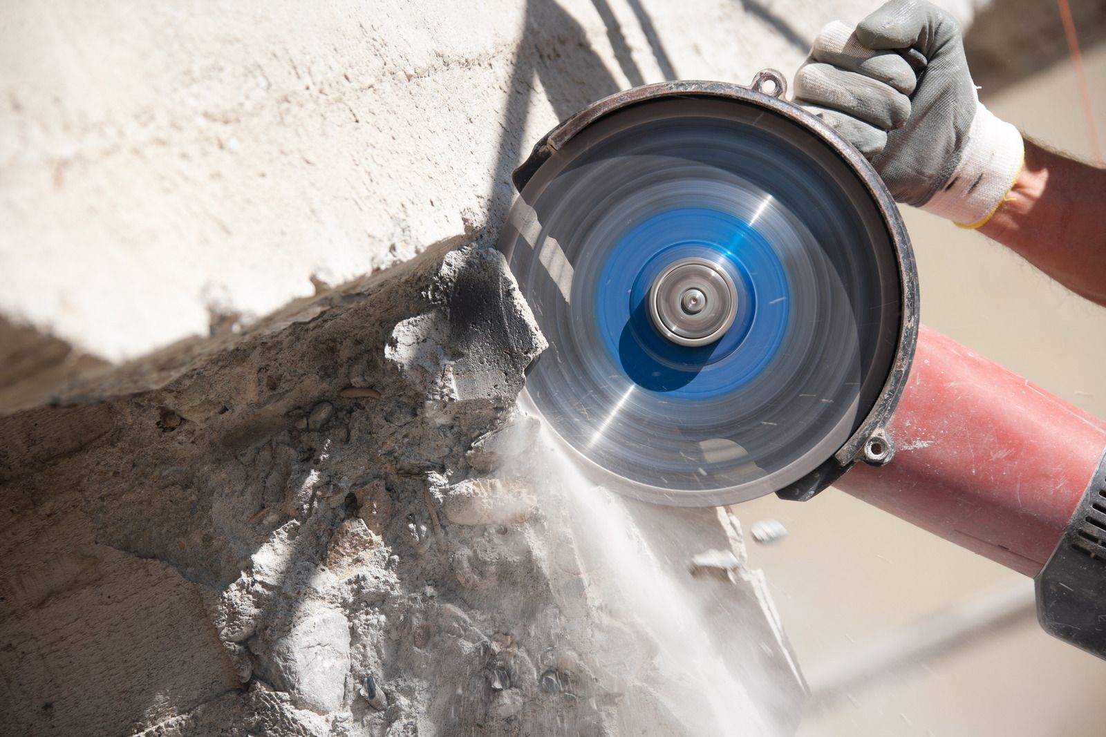 Person using a power saw, cutting concrete; emitting dust.