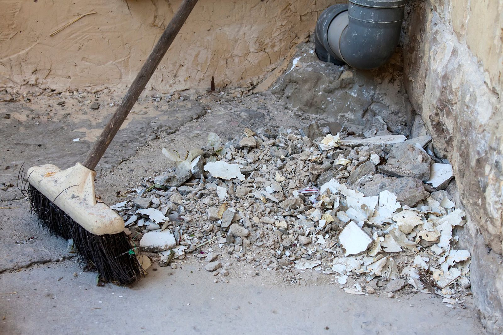 A broom is sitting on the ground next to a pipe.