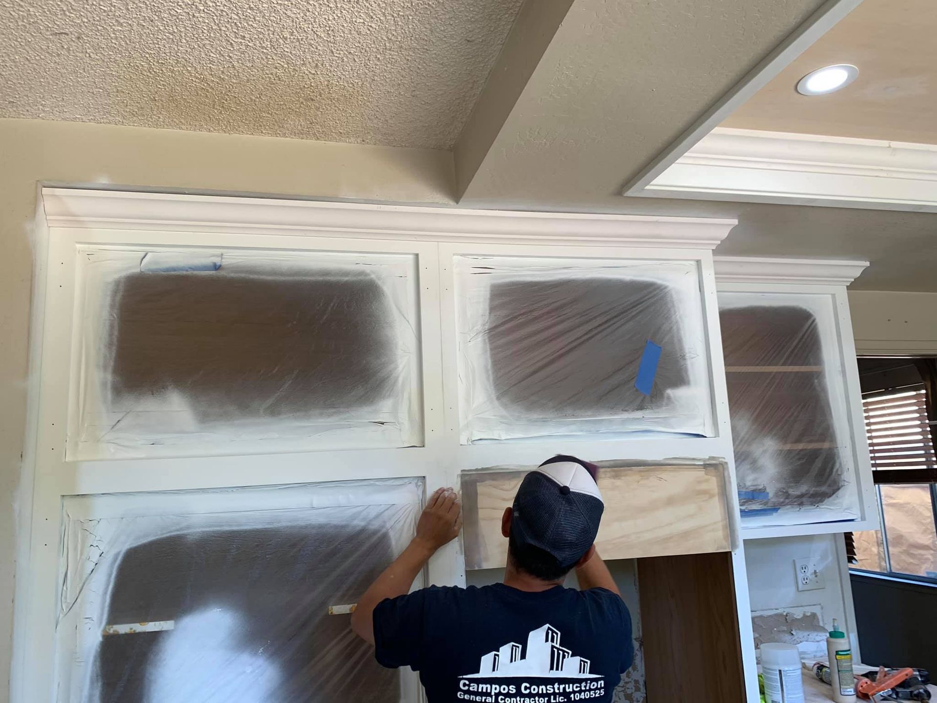 A man in a blue shirt is painting cabinets in a kitchen.