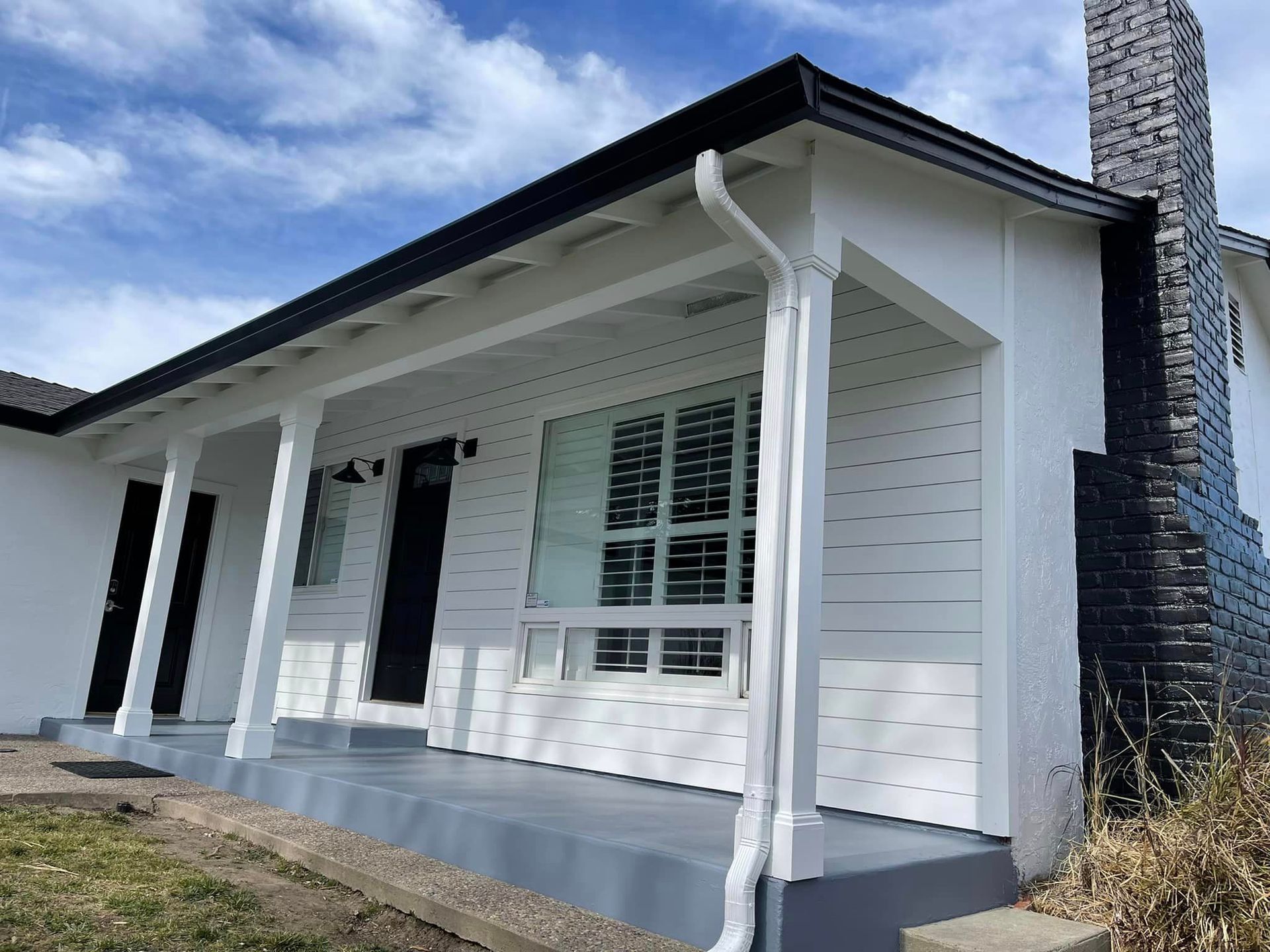 A white house with a black chimney and a porch