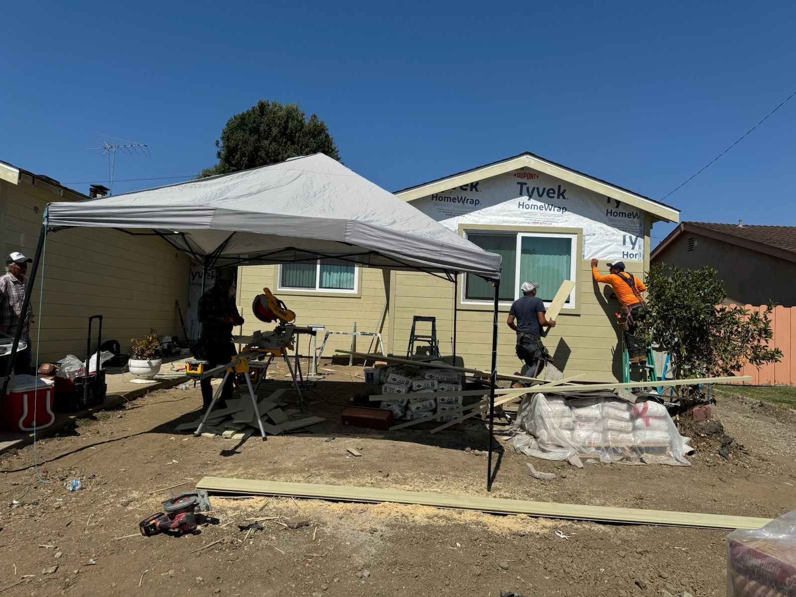 A group of people are working on a house under a tent.